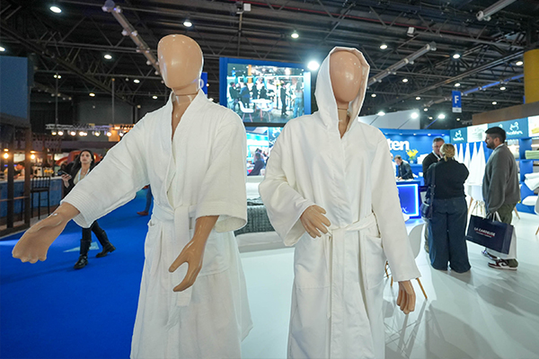 Exhibición de batas y textiles para hotelería en un stand de la exposición Hotelga, destacando equipamiento profesional para el sector.