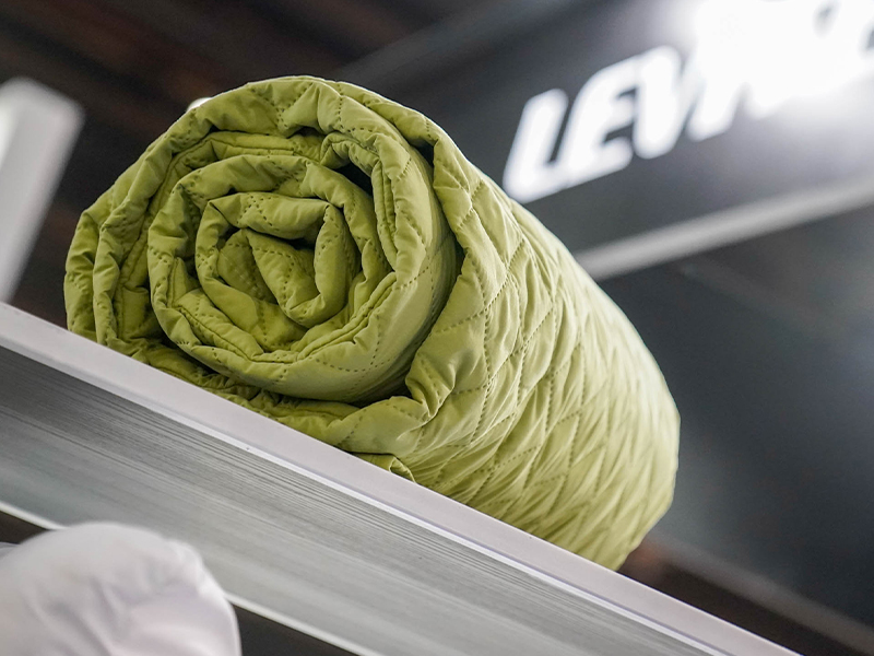 foto de Acolchado o cubrecama verde enrollado, expuesto como producto textil para hotelería en Hotelga.