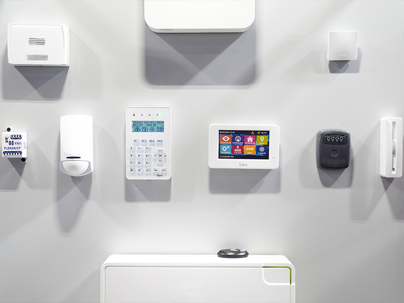 Una pared blanca con una variedad de dispositivos de control para el hogar inteligente instalados, incluyendo un teclado numérico, un panel de control con pantalla táctil, sensores y otras unidades de alarma.