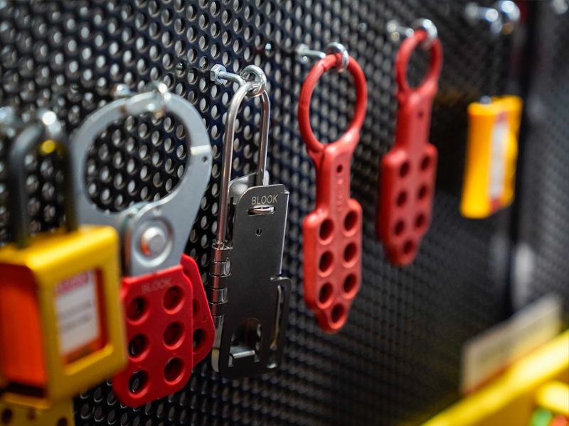 varios candados y dispositivos de seguridad para bloqueo y etiquetado en diferentes colores, colgados en un panel metálico perforado.