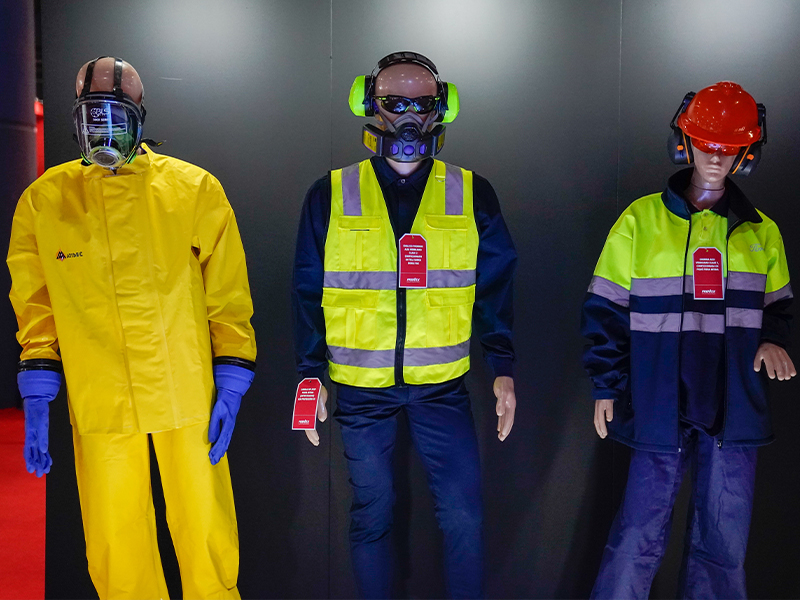 tres maniquíes vestidos con diferentes tipos de equipo de protección personal (EPP) de seguridad industrial, incluyendo un traje amarillo, un chaleco de alta visibilidad y un uniforme de trabajo con casco.