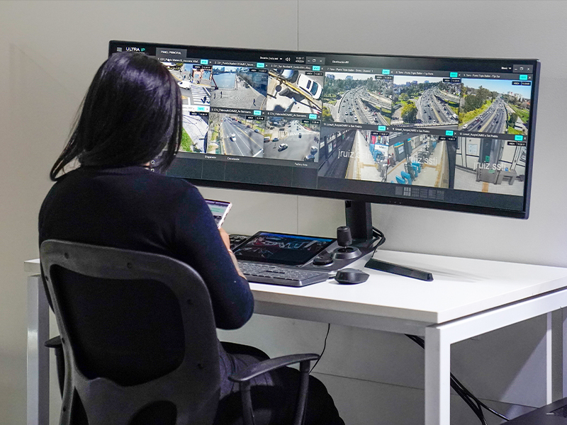 Una persona sentada de espaldas a la cámara, mirando una gran pantalla de monitor curvo que muestra varias cámaras de videovigilancia de tráfico en vivo.