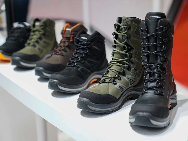 Un primer plano de una fila de botas de senderismo resistentes en varios colores (verde, marrón, negro), mostradas en un estante blanco en Intersec BA.