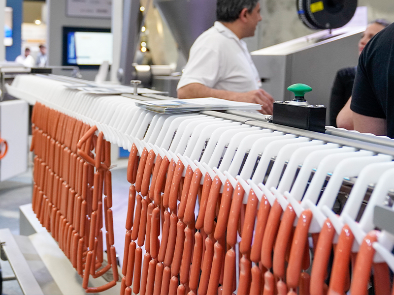 Un primer plano de una máquina de procesamiento de alimentos que cuelga y organiza salchichas en filas